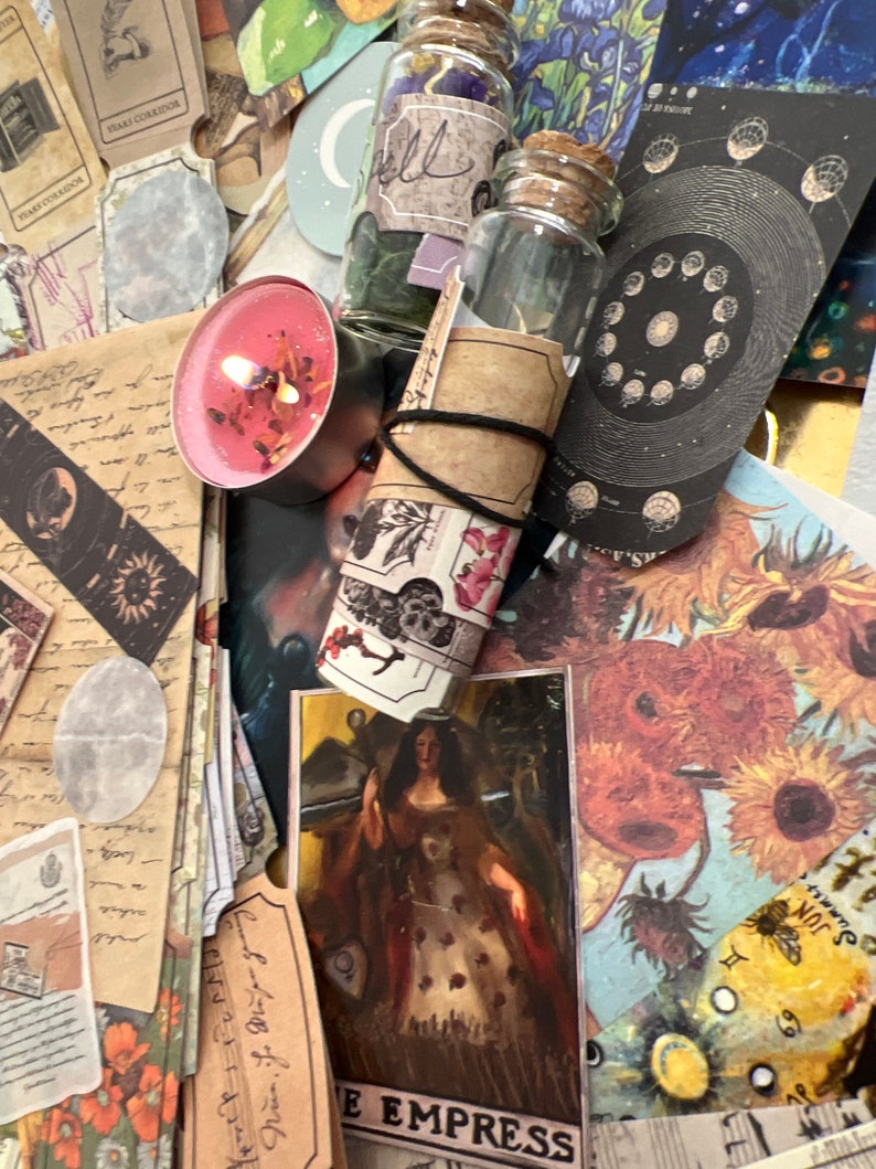 Puede incluir: Una colecci&oacute;n de objetos m&iacute;sticos que incluyen cartas del tarot, peque&ntilde;os frascos de vidrio con tapones de corcho, una vela rosa encendida y papel decorativo. La carta del tarot "The Empress" es visible. Los objetos est&aacute;n dispuestos sobre una superficie con una variedad de colores y texturas.