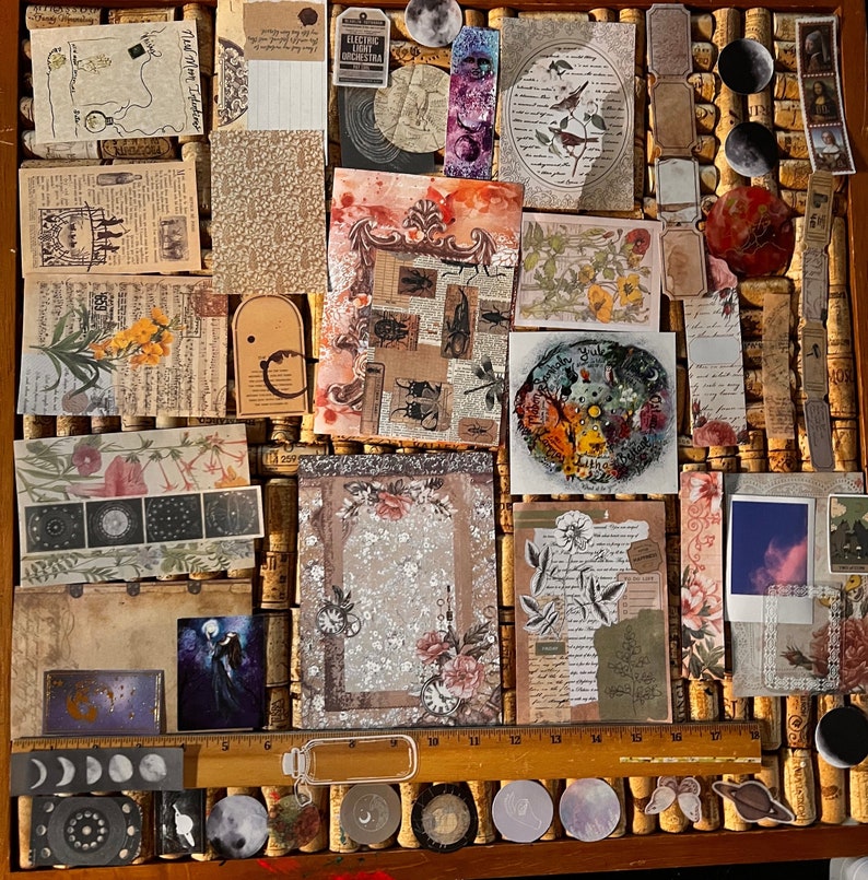 Puede incluir: Una colecci&oacute;n de ef&iacute;meras de estilo vintage, que incluye recortes de papel, pegatinas y etiquetas, dispuestas en un corcho. Los art&iacute;culos presentan temas bot&aacute;nicos, celestiales e insectos, con una paleta de colores beige, marr&oacute;n y tonos apagados. Una regla est&aacute; colocada en la parte inferior.