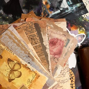 Può includere: Una collezione di ephemera di carta vintage con una varietà di disegni, tra cui farfalle, fiori e pizzi. Le carte sono in tonalità di marrone, beige e bianco, e hanno un aspetto usurato e invecchiato.