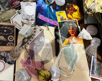 May include: A collection of vintage and modern ephemera, including a clear glass bottle, a pink butterfly, and a card with a woman wearing a crown of flowers. The ephemera is arranged on a brown surface with a white background.
