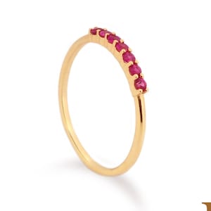 Könnte beinhalten: Ein zarter Goldring mit einer Reihe leuchtend roter Edelsteine. Das schmale Band des Rings und die leuchtend roten Steine bilden einen auffälligen Kontrast. Der Ring ist ein feines Schmuckstück.