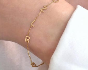 May include: A delicate gold bracelet featuring the letters R, L, Z, and O. The bracelet is worn on a wrist, with a white shirt in the background. The jewelry is from Fine Jewelry Lab.