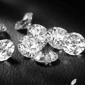 May include: Close-up, black and white image of several round-cut diamonds. The diamonds are scattered on a dark surface, with light reflecting off their facets. The image highlights the brilliance and clarity of the gemstones.