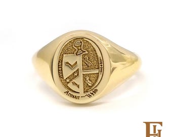 May include: A gold signet ring featuring an oval face with an engraved heraldic crest. The design includes a shield divided into quadrants with bird and chevron motifs, topped with a helmet. The text Armour - With is engraved below.