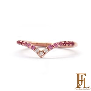 May include: A V-shaped rose gold ring featuring a gradient of round-cut pink and red gemstones along the band, with three clear white stones set at the center point. The band has a polished finish and a delicate, curved silhouette.
