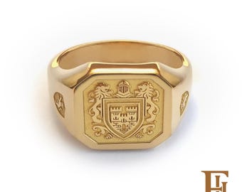May include: A gold signet ring with a detailed crest featuring a shield, lions, and a helmet. The ring has an octagonal face and a polished finish, showcasing a classic design.