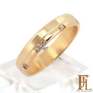 Puede incluir: Un anillo dorado con pequeños diamantes. El anillo tiene una superficie lisa y pulida con un diseño de ranura sutil. El anillo se muestra sobre una superficie clara e inclinada. El logotipo "Fine Jewelry Lab" es visible.