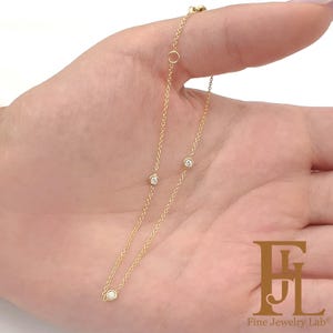 May include: A delicate gold chain necklace with three small round diamonds. The necklace is on a hand, and the chain is visible in the background.