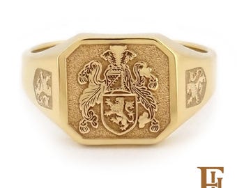 May include: A gold signet ring with a detailed family crest. The ring features a rectangular face with an engraved coat of arms, including a lion rampant. The band has a polished finish, and the ring is set against a white background.