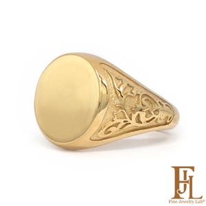 May include: A gold signet ring featuring a smooth, polished circular face and intricate, raised scrollwork detailing along the sides of the band. The ring has a warm, metallic yellow finish and a tapered design that narrows towards the back.