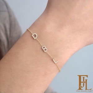 May include: A delicate gold bracelet with the letters D, B, and L, each encrusted with small, sparkling stones. The bracelet is worn on a wrist, showcasing the personalized design. The Fine Jewelry Lab logo is visible in the bottom right corner.