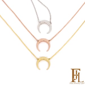 Può includere: Tre collane con pendenti a forma di corno in argento, oro rosa e oro giallo. Ogni collana presenta una delicata catena e un pendente a forma di mezzaluna. I pendenti hanno una finitura liscia e lucida. Le collane sono esposte su sfondo bianco.