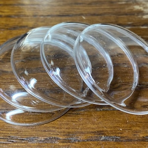 Peut inclure: Un ensemble de quatre cabochons en verre transparent, circulaires et en forme de dôme, avec des surfaces lisses et polies. Chaque pièce présente un dessus convexe et un fond plat, conçus avec une finition transparente laissant passer la lumière.