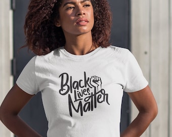 Puede incluir: Una camiseta blanca con el texto "Black Lives Matter" en letras negras y un gráfico de puño en alto.