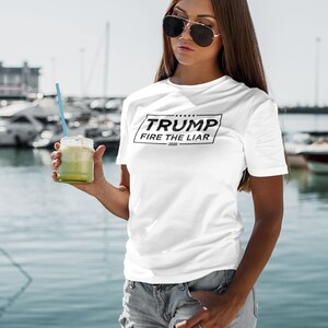 May include: White t-shirt with a black square graphic that says "TRUMP FIRE THE LIAR 2020".