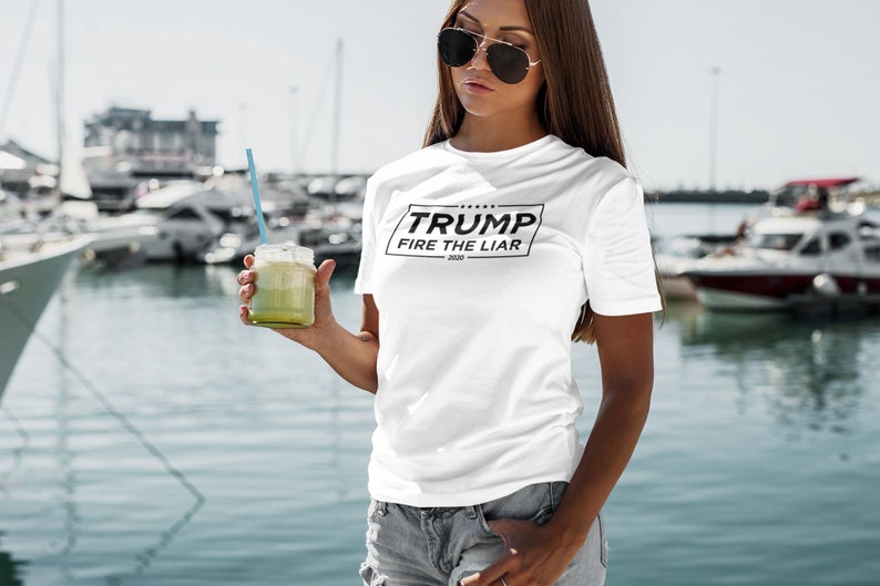 May include: White t-shirt with a black square graphic that says "TRUMP FIRE THE LIAR 2020".