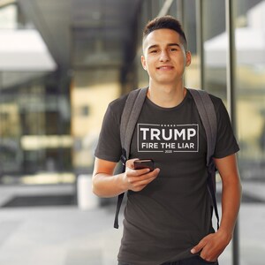 May include: A dark gray t-shirt with a white rectangle on the front that says "TRUMP FIRE THE LIAR 2020".