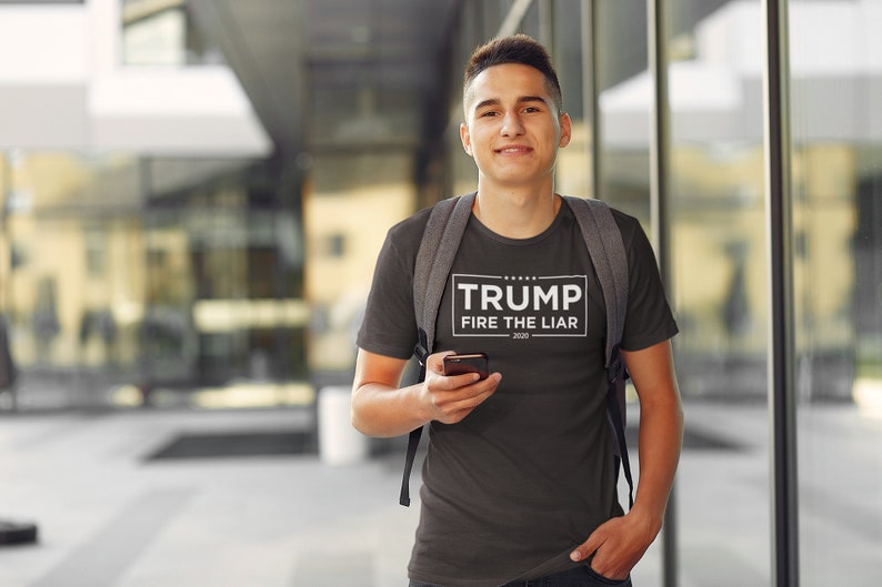 May include: A dark gray t-shirt with a white rectangle on the front that says "TRUMP FIRE THE LIAR 2020".