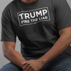 May include: A black t-shirt with a white rectangle that says "TRUMP FIRE THE LIAR - 2020" in all caps.