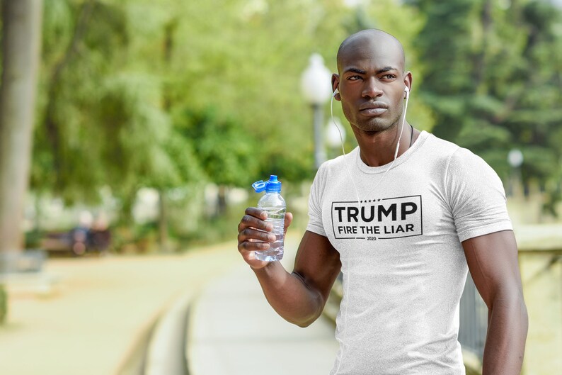 May include: A white t-shirt with a black rectangle on the front that says "TRUMP FIRE THE LIAR 2020". A person is wearing the shirt and holding a clear water bottle.