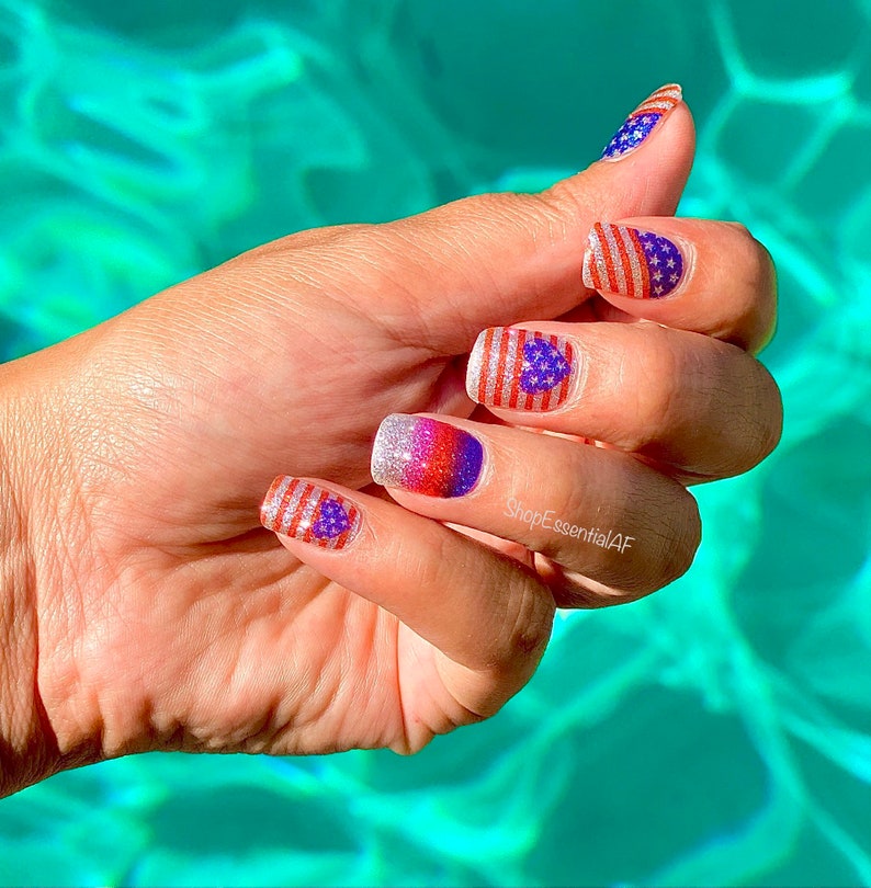 Peut inclure: Gros plan sur une main avec quatre ongles peints d'un vernis &agrave; ongles paillet&eacute; rouge, blanc et bleu avec un petit motif de drapeau am&eacute;ricain. La main repose sur une surface turquoise.