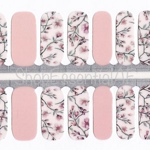 May include: A sheet of nail polish wraps with a floral design. The wraps feature a white background with pink and gray floral branches. The wraps are designed to be applied to fingernails.