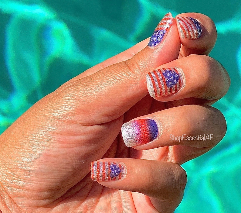 Peut inclure: Gros plan sur une main avec un nail art rouge, blanc et bleu repr&eacute;sentant des drapeaux am&eacute;ricains. Les ongles sont peints avec une base de paillettes argent&eacute;es et ont un effet ombr&eacute; rouge, blanc et bleu. Le texte "ShopEssentialAF" est visible sur la main.