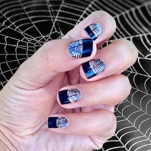 May include: Close-up of a hand with black nail polish and white spiderweb nail art designs. The hand is in front of a black and white spiderweb background.