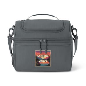 May include: A gray insulated lunch bag with a top handle, shoulder strap, and a front pocket. The bag features a rectangular patch with the words "Camping & Chaos" above a sunset scene with trees and water.