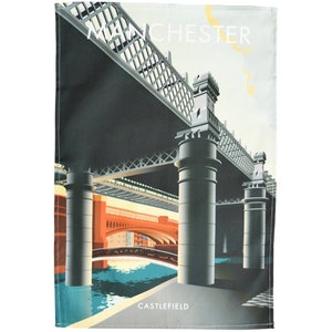 May include: A tea towel featuring a stylized illustration of a bridge in Manchester, England. The design includes the text "MANCHESTER" and "CASTLEFIELD" in white. The artwork uses a palette of gray, orange, and blue.
