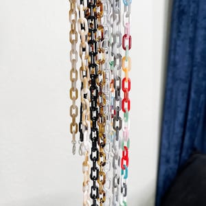 May include: A collection of colorful acrylic chain links in various shades, including white, black, brown, gray, red, and pink. The chains are hanging, showcasing their individual colors and textures. The links are connected, forming a chain.