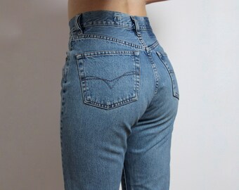 May include: Light blue denim jeans with a classic five-pocket design. The jeans have a high waist and a straight leg cut. The back pocket features a decorative stitch. The jeans are made of a medium-weight denim fabric.