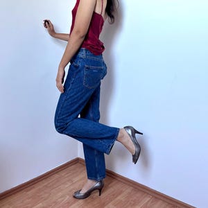 May include: A dark red satin camisole with thin straps paired with medium-wash blue denim jeans featuring a classic five-pocket design and a straight-leg cut, worn with metallic silver peep-toe heels with a mid-height stiletto heel.
