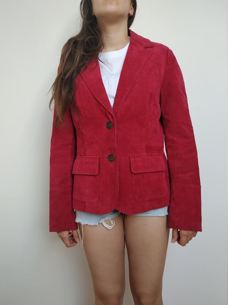 K&ouml;nnte beinhalten: Ein roter Wildlederblazer mit Knopfleiste und zwei Pattentaschen. Der Blazer hat lange &Auml;rmel und eine figurbetonte Silhouette.