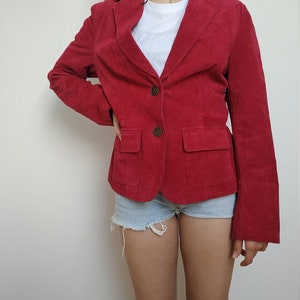 K&ouml;nnte beinhalten: Ein roter Wildlederblazer mit einem Reverskragen, einem Zwei-Knopf-Verschluss und einer einzigen Pattentasche auf der linken Seite.