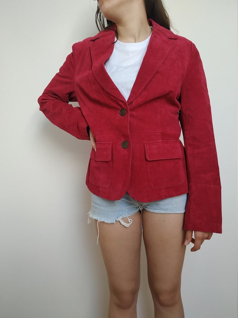 K&ouml;nnte beinhalten: Ein roter Wildlederblazer mit einem Reverskragen, einem Zwei-Knopf-Verschluss und einer einzigen Pattentasche auf der linken Seite.