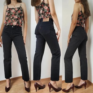 Könnte beinhalten: Eine schwarze gerade Jeans mit hoher Taille. Die Jeans wird von einer Person getragen, die ein Blumen-Oberteil und braune Absätze trägt.