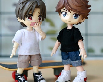 May include: Two small dolls wearing casual outfits. The doll on the left is wearing a white t-shirt, gray shorts, and black and red sneakers. The doll on the right is wearing a black t-shirt, blue denim shorts, and white sneakers with red hearts.