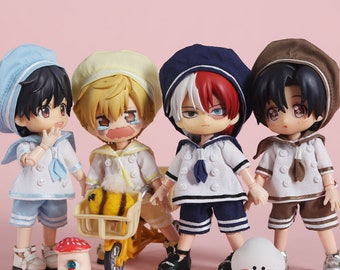 May include: Four small sailor-themed dolls with different colored hair and outfits. The dolls are wearing white sailor shirts with blue trim, blue and white striped shorts, and sailor hats. The dolls are standing on a pink surface with a small yellow toy tricycle and a mushroom-shaped toy.