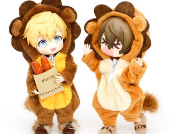 May include: Two plush lion costumes for dolls. The costumes are brown and tan with a zipper closure. One doll is holding a brown paper bag with the word "BREAD" printed on it.