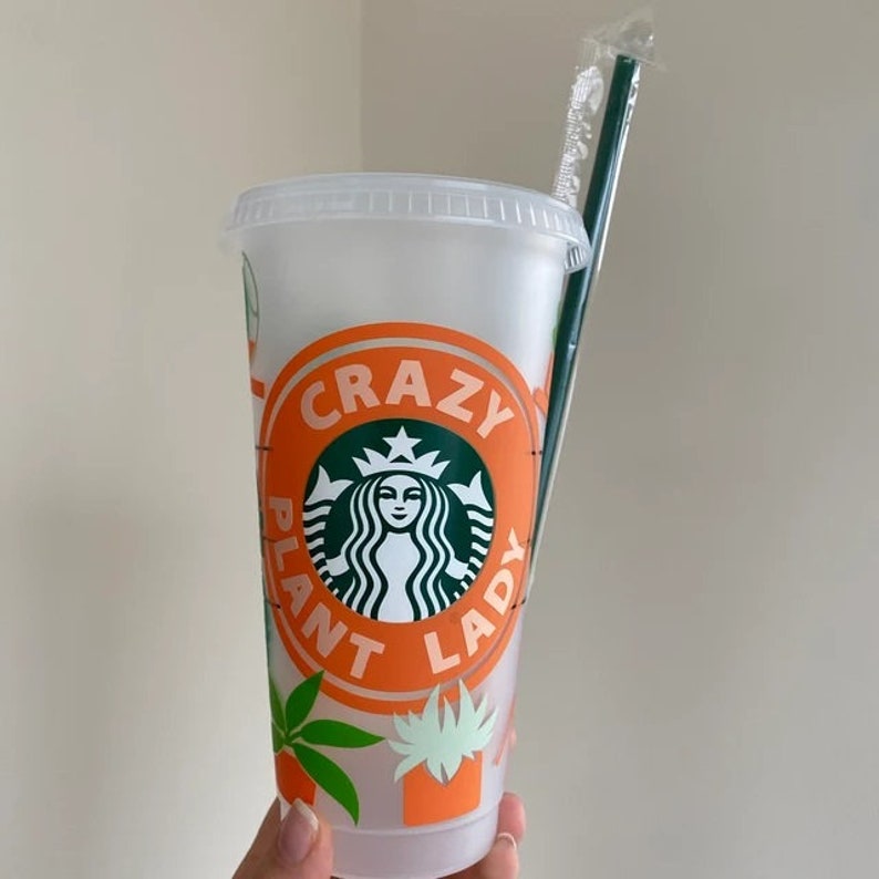 May include: A clear plastic reusable cup with a green Starbucks logo and the text "Crazy Plant Lady" in orange. The cup has a green straw and a design of green plants on the side.