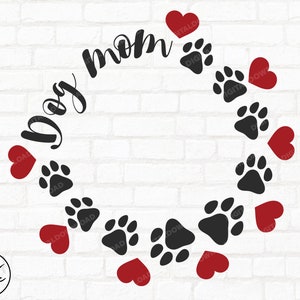 May include: A black and white graphic design of a paw print wreath with red hearts around it. The text "Dog Mom" is written in a cursive font around the wreath.
