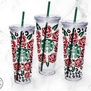 Peut inclure: Trois gobelets en plastique transparent avec couvercles et pailles. Chaque gobelet pr&eacute;sente un motif diff&eacute;rent avec des roses rouges, des feuilles vertes et un imprim&eacute; l&eacute;opard noir et blanc. Les gobelets sont sur une surface en marbre blanc.