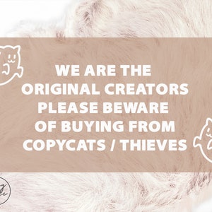 May include: A light brown background with white text that reads "WE ARE THE ORIGINAL CREATORS PLEASE BEWARE OF BUYING FROM COPYCATS / THIEVES". There are two white ghost illustrations on either side of the text.