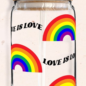 May include: A glass jar with a wooden lid and a glass straw. The jar has a rainbow design with the text "Love is Love" repeated on the jar.