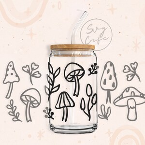 May include: A clear glass jar with a wooden lid and a black straw. The jar is decorated with black line drawings of mushrooms and leaves. The jar is sitting on a white background.