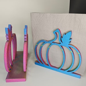May include: Two wooden pumpkin napkin holders. One is pink with iridescent glitter and the other is blue with iridescent glitter.