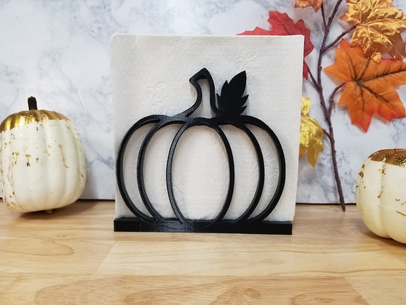 May include: Black metal pumpkin-shaped napkin holder. The holder is designed to hold a stack of napkins upright.