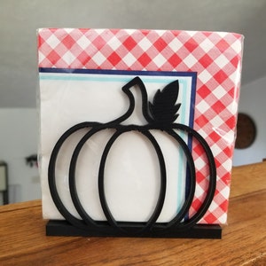 May include: Black metal pumpkin-shaped napkin holder with a red and white checkered napkin inside.