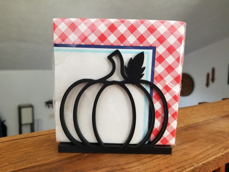 May include: Black metal pumpkin-shaped napkin holder with a red and white checkered napkin inside.